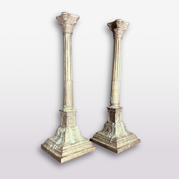 A pair of vintage-style Corinthian pillar candlesticks with fluted shafts and square bases, shown on a light gray gradient background.