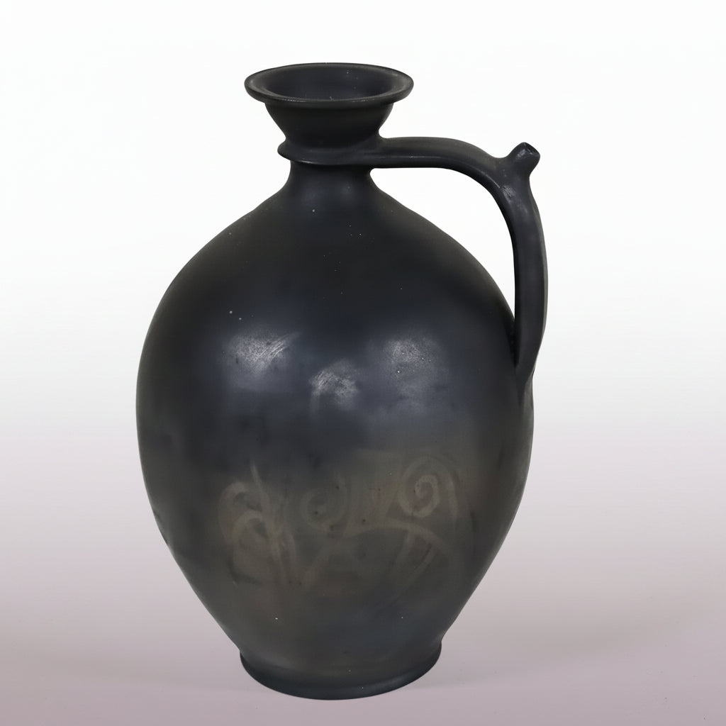 A striking antique French gargoulette in dark charcoal-black terracotta, distinguished by its generous ovoid body and elegantly curved handle terminating beside the neck.