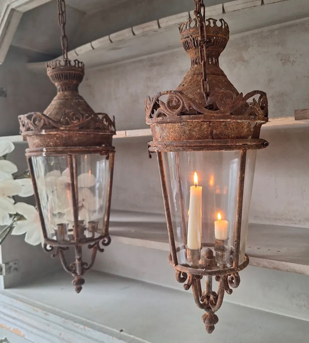 Two ornate hanging lanterns with glass covers and candles inside, hanging from a ceiling.