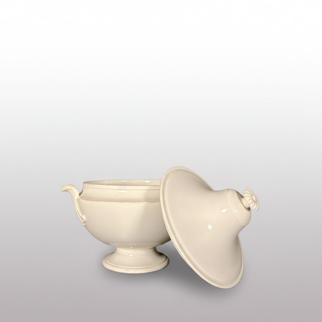 A white ceramic tureen with a matching lid leaning against it, set on a dark surface against a dark gray backdrop.