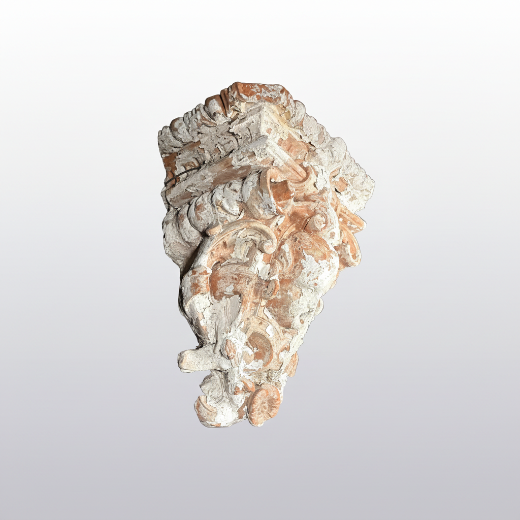 An ornate carved stone or plaster decorative fragment with a weathered, aged appearance in off-white and warm tan tones, isolated on a plain white background.