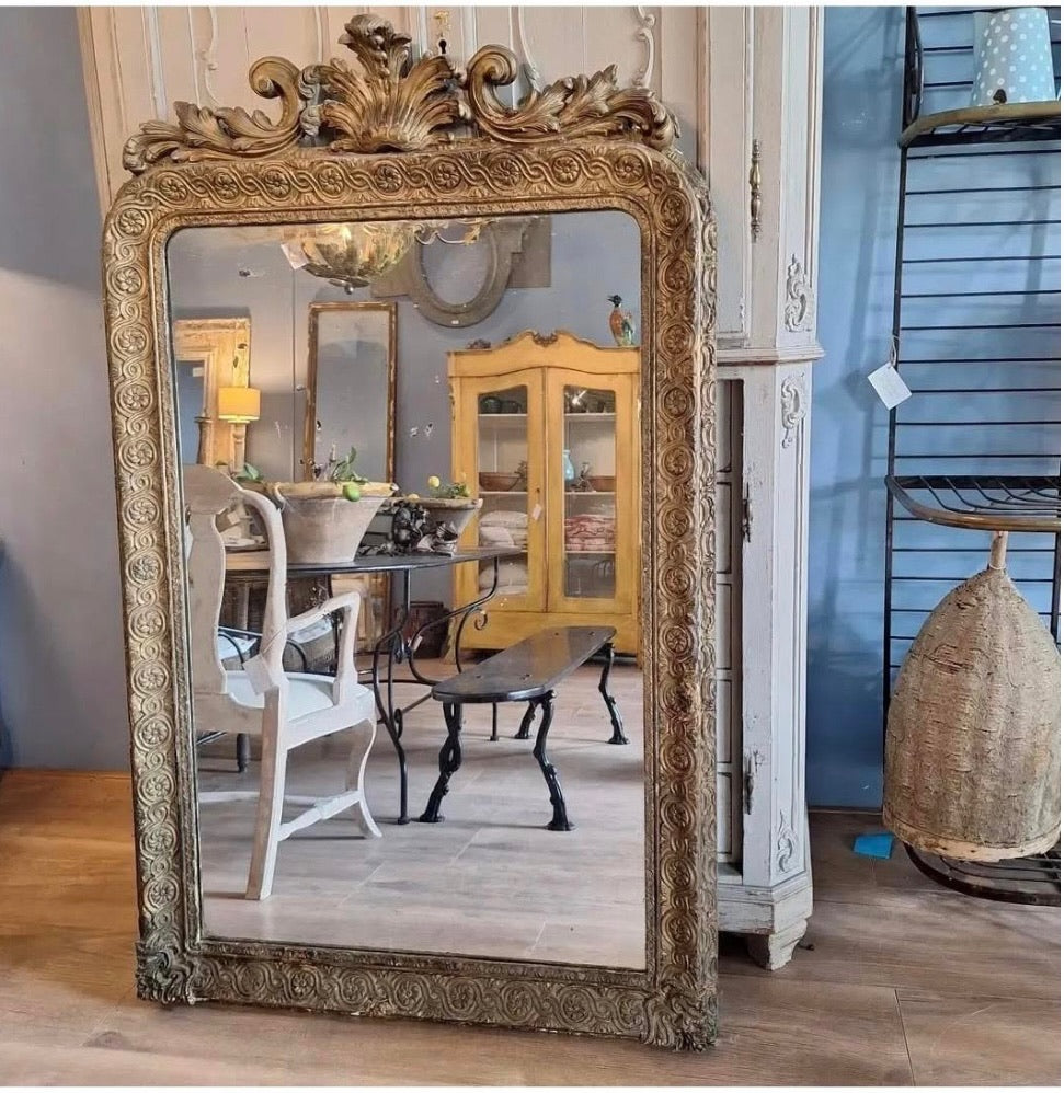 Decorative gold-framed mirror in a room with furniture and decor.