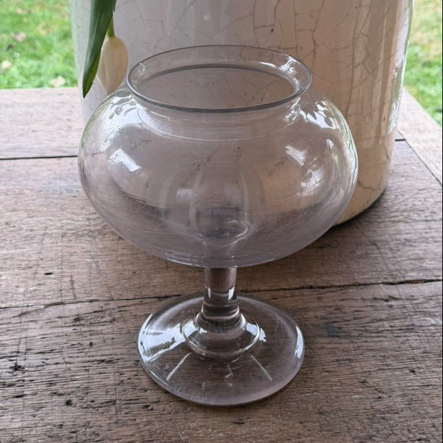 Clear glass vase on a wooden surface with a plant pot in the background