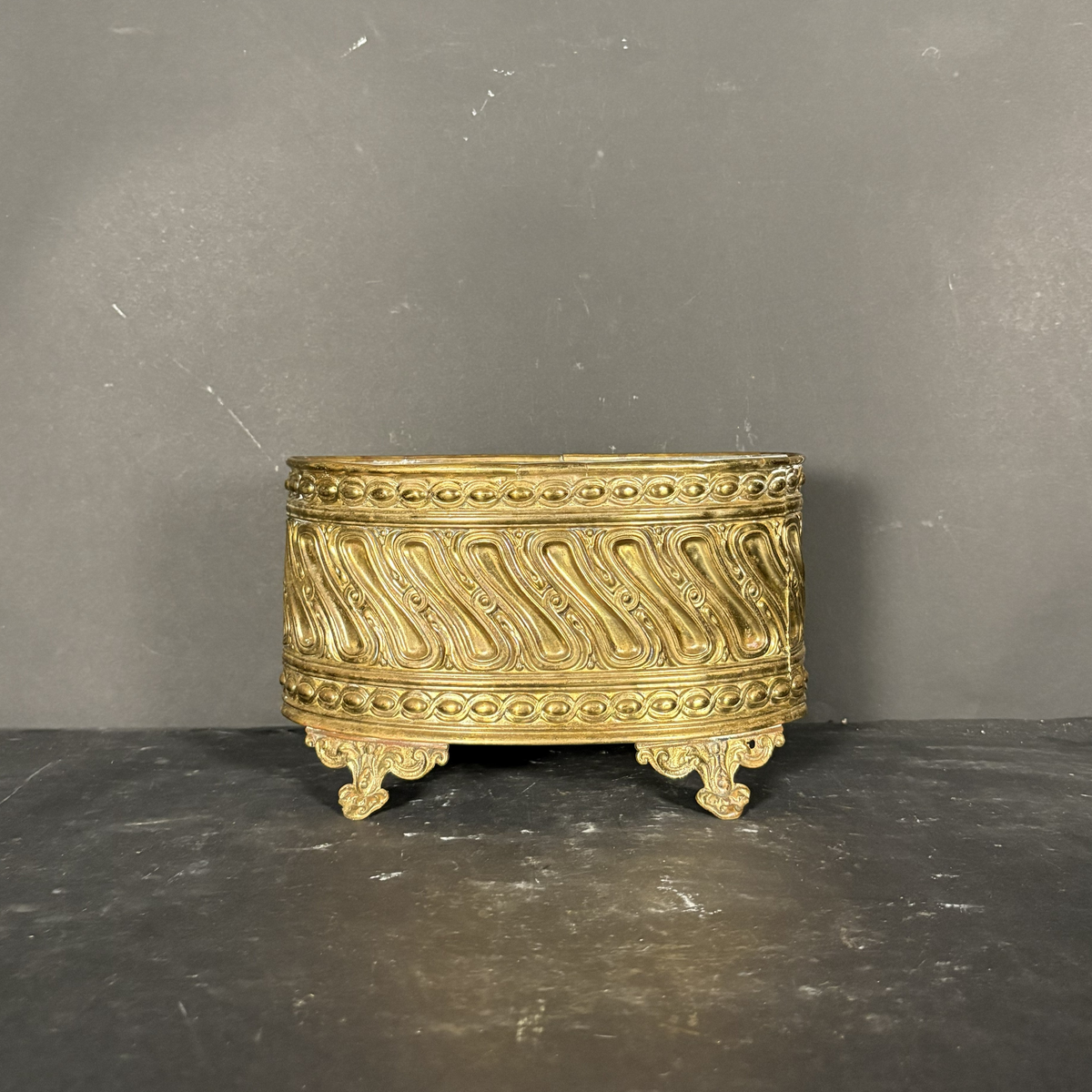 An ornate gold-colored metal decorative box with intricate scrollwork and claw feet, set against a dark gray background.