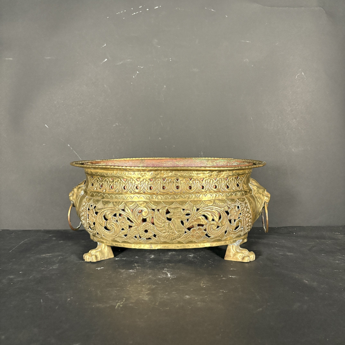 An ornate antique-style gold metal incense burner with intricate filigree cutouts and lion head feet, set against a dark gray backdrop.