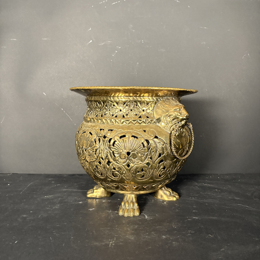 An ornate antique-style gold metal incense burner with intricate filigree cutouts, a side ring handle, and three claw feet, set against a dark gray background.
