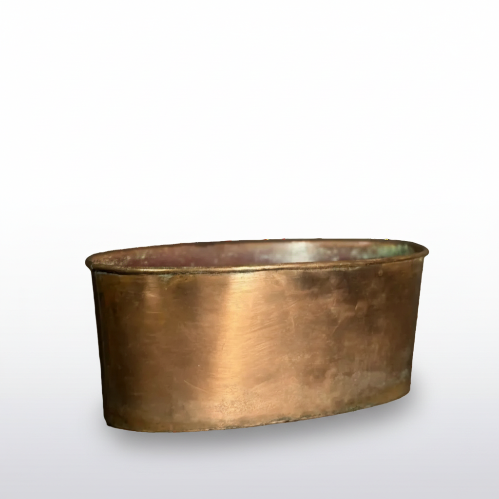 A small oval copper-colored metal container or tray with a brushed metallic finish, shown on a dark surface against a dark gray background.