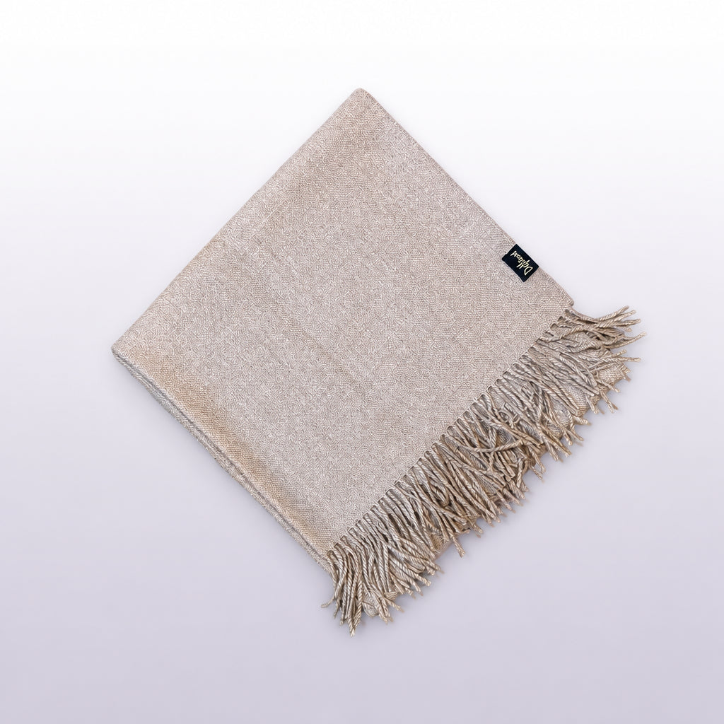 A folded dusty pink woven scarf with fringe detailing, displayed diagonally on a rustic wooden surface. A small black brand tag is visible near one corner.