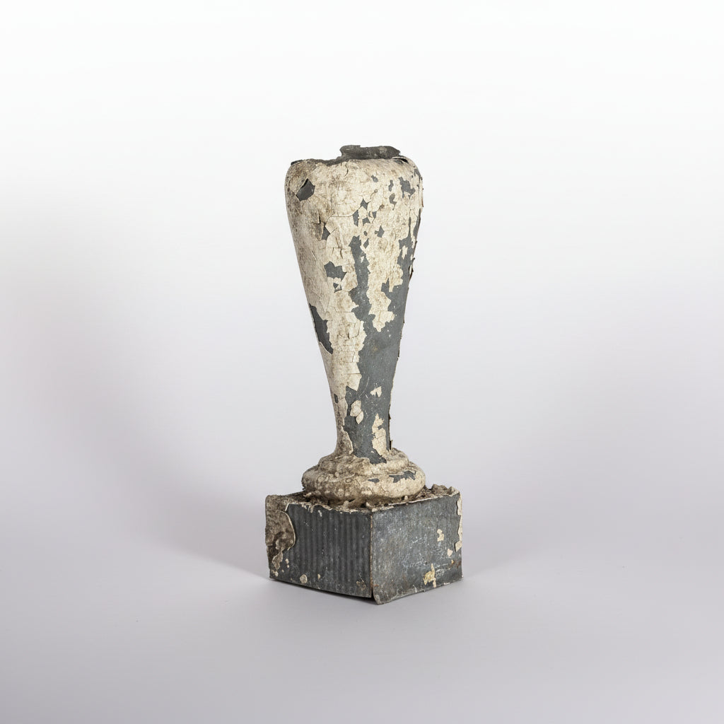 An antique ceramic vase with a heavily distressed, peeling white glaze over a dark gray body, displayed on a matching dark base against a black background.